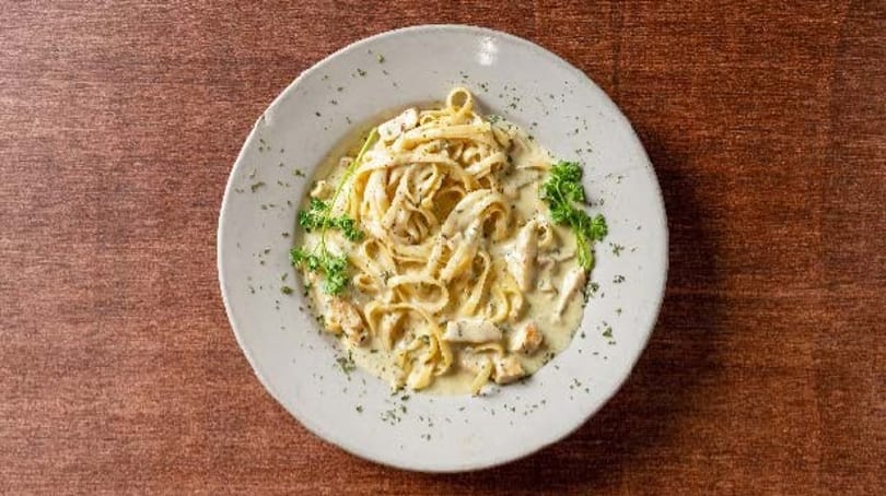 Creamy fettuccine alfredo with chicken and parsley on a white plate, on a wooden table.