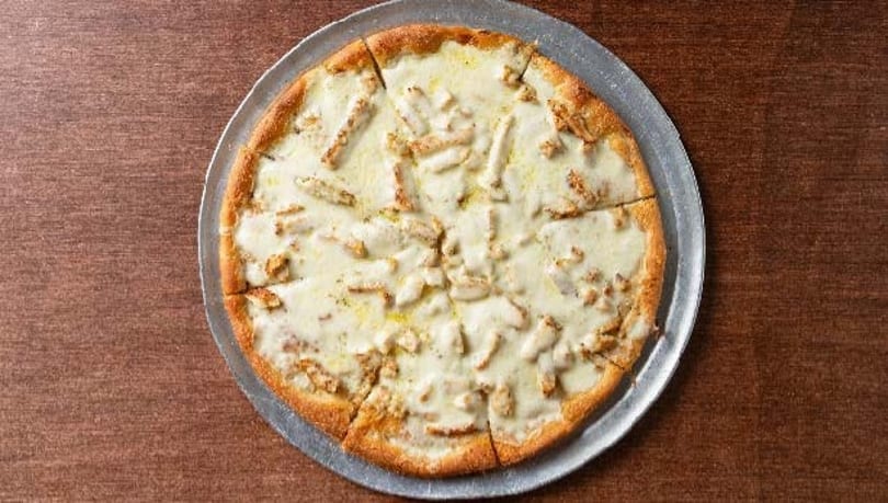 Whole white pizza with chicken pieces on a metal tray, on a wooden table.