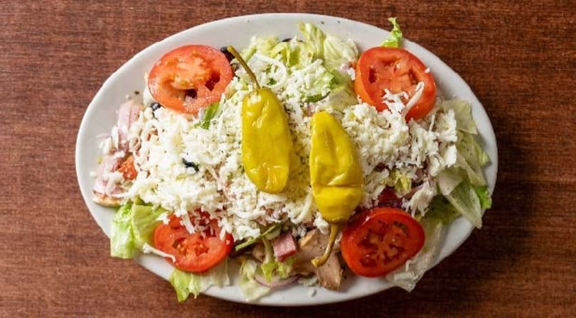 A large salad with lettuce, tomatoes, cheese, and two yellow peppers on a white plate.