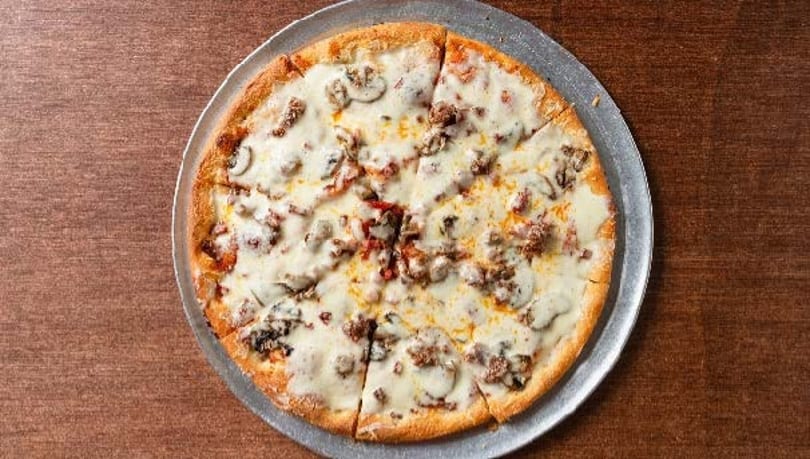 A whole white pizza with mushrooms and sausage, sliced and served on a metal pan.