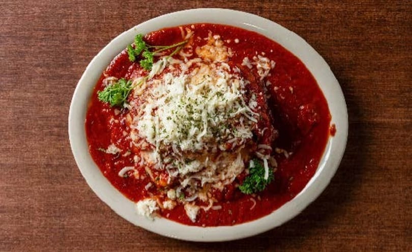 Chicken Parmesan with marinara sauce, melted cheese, and parsley on a white plate.